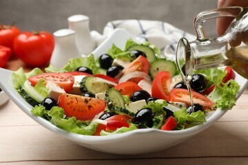Adding olive oil to Greek salad at white wooden table, closeup