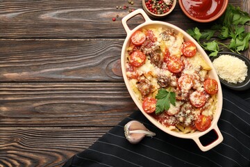 Delicious pasta casserole in baking dish with ingredients and sauce on wooden table, flat lay. Space for text