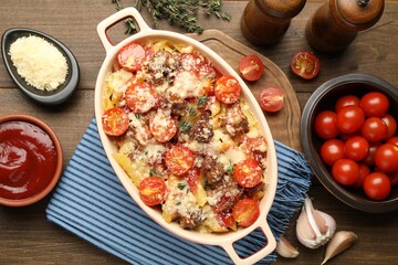 Delicious pasta casserole in baking dish with ingredients on wooden table, flat lay