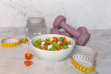 Healthy lifestyle concept with salad bowl, water, dumbbells and measuring tape. Diet concept.  