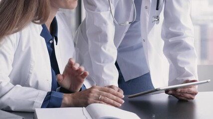 Two women doctors dressed in uniforms, engaged in patient care discussion, analyzing medical data using digital tablet, close up. Collaborative meeting, professional opinion exchange, teamwork, tech - Powered by Adobe