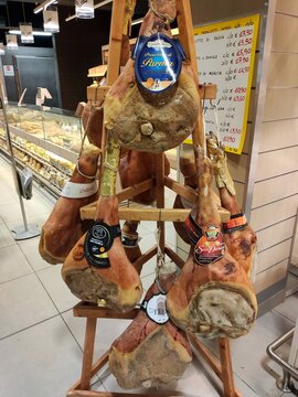 Traditional Italian cured prosciutto ham legs hanging on wooden display stand inside grocery store shop in province of Teramo Abruzzo region landscape Italy.