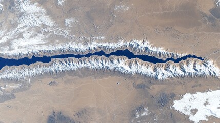 Aerial view of a mountainous region with snow-capped peaks and a deep blue body of water.