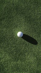 White golf ball sits on a vibrant green putting green, casting a distinct shadow under the bright sunlight, creating a serene and focused golfing scene