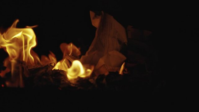 Burning documents in a fireplace, with vibrant flames consuming the papers, intense and dramatic scene. Filmed in 4K, the glowing fire illuminates the dark surroundings. getting rid of evidence.