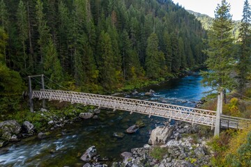 Wooden suspension bridge spans a rushing river, nestled in a lush forest. Nature's beauty. Lochsa River, Lowell, Idaho, USA.