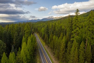 Obraz premium High-angle view of a winding road through a lush green forest, leading to snow-capped mountains. Scenic route. , Seeley Lake, Montana, USA.