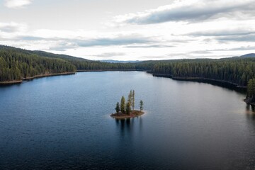 Obraz premium Tranquil lake with small island, surrounded by forest. Calm water reflects the surrounding trees. Peaceful nature scene. Salmon Lake, Seeley Lake, Montana, USA.