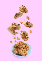 Yummy nut cookies falling onto plate on pink background