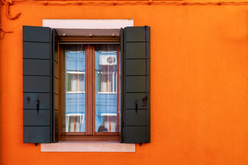 Italy, Burano. Colorful buildings the island is known for.  Orange wall with black shutters.