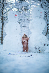shih tzu dog stands near snowmen in the forest in winter