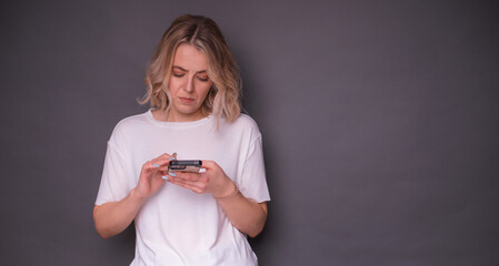 A young woman in a white t-shirt looks at her smartphone with a confused expression against a...