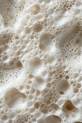 Close-up of a creamy, bubbly texture; a myriad of air pockets create a captivating, almost lunar-like landscape in off-white tones.