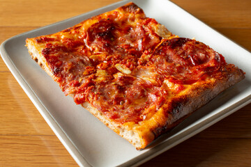A view of a Sicilian style salami pizza slice.