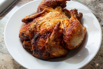 A view of a whole rotisserie chicken on a plate.