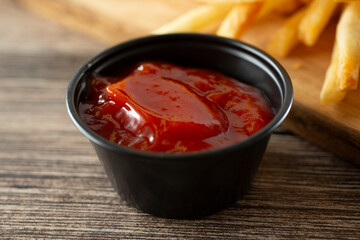 A closeup view of a black plastic condiment cup of ketchup.
