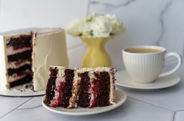Chocolate cake with creamy frosting and raspberry filling served on white plate with cup of coffee, set against.