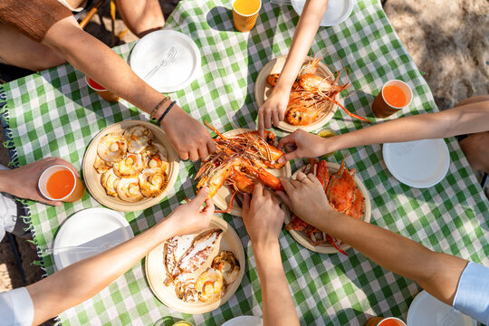 Happy man and woman travel at the sea on summer beach holiday vacation. Group of Asian people friends enjoy and fun outdoor lifestyle having lunch eating seafood together on tropical island beach.
