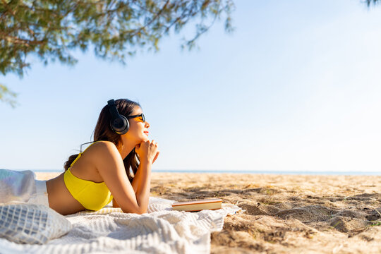 Happy Asian woman travel the sea on summer beach holiday vacation. Attractive girl enjoy outdoor lifestyle travel nature, social media detox relaxing, reading book and listening to music on the beach.