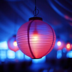 Fototapeta premium Illuminated pink paper lantern hanging indoors with blue background.