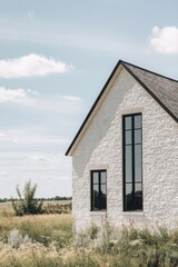 Fototapeta premium A contemporary white house sits peacefully within a tranquil landscape, surrounded by lush green grass and a bright blue sky during the day