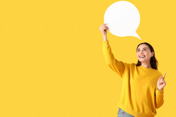 Young woman with blank speech bubble pointing at something on yellow background