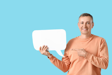 Mature man pointing at blank speech bubble on blue background