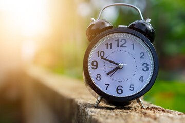 A close-up of a black alarm clock on a stone surface, bathed in soft morning light.
