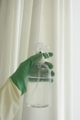 A Cleaning Spray Bottle held in a Gloved Hand, used to care for White Curtains