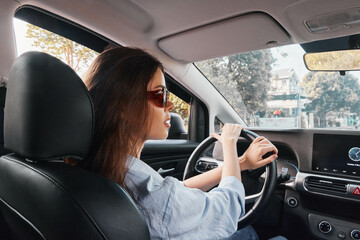 Fototapeta premium Woman driving car, hands on steering wheel, eyes focused on car's infotainment screen, interior view, daylight, modern technology usage, attentive driver, transportation concept