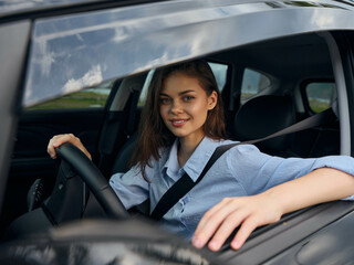 young woman in driver seat with hand on steering wheel, looking at camera, inside a car interior,...