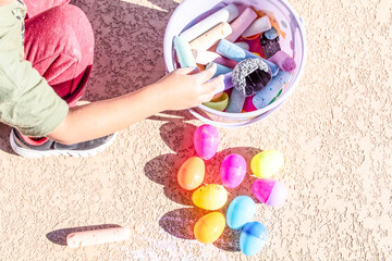 Toddler playing outdoors with colorful easter eggs and chalk