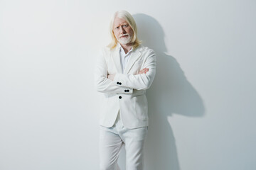 Older man with long white hair wearing a stylish white suit, standing confidently against a...