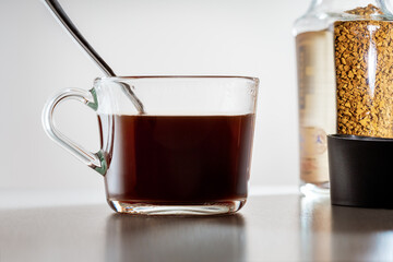  close-up of black coffee in a clear glass mug and instant coffee in a glass jar on the table.