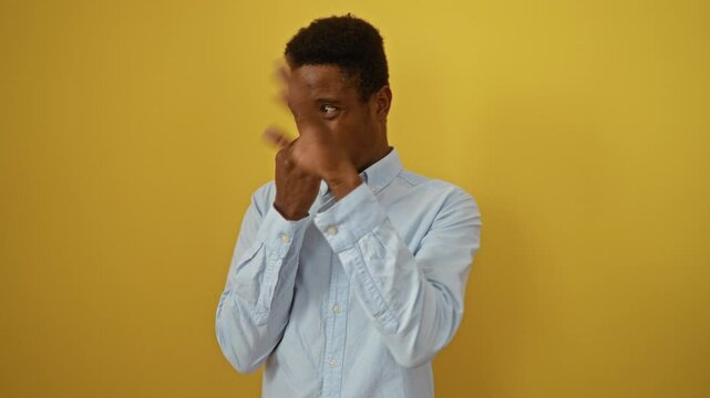 Young african american man wearing shirt standing against a yellow background holding nose due to intolerable stinky and disgusting smell in the air