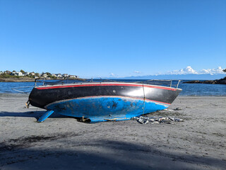 A derelict sail boat sits on a beach near expensive houses in Victoria BC Canada after being washed...