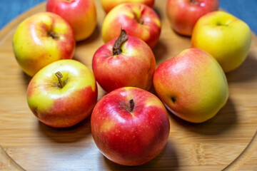 Beautiful fresh juicy red and yellow garden apples lie on a round bamboo cutting board.