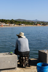 Panorama of the beach in Jalisco, Mexico in which a fisherman can be seen catching fish from the beach boardwalk