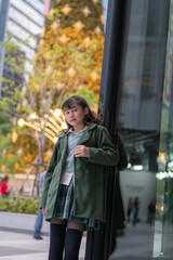 Obraz premium A young girl in a green coat posing gracefully in a festive urban setting, with a glowing Christmas tree and sparkling lights in the background, capturing a serene and joyful holiday moment.