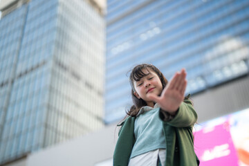 A confident young woman in a green coat standing outdoors, looking upward against the backdrop of a...