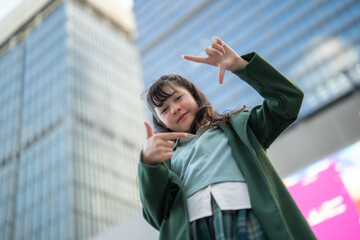 A confident young woman in a green coat standing outdoors, looking upward against the backdrop of a...