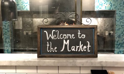 Chalkboard sign on counter top reading welcome to the market