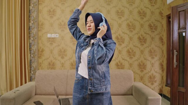 Young Muslim girl enjoying her favorite music while relaxing at home. Swaying gently to the rhythm of the beats in her cozy room. Headphones, music, joy, relaxation, comfort home