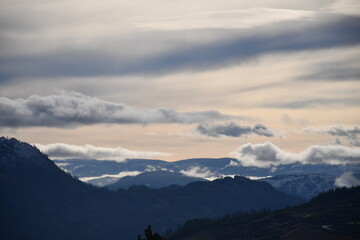 Paisaje montañoso al amanecer. Capas de nubes bajas sobre montañas silueteada. Tonos suaves, atmosférico y sereno.  Impresiona la calma y la inmensidad del paisaje.