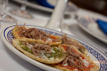 Chalupas poblanas, red and green salsa, served on a Talavera plate with intricate blue filigree, in a fine dining atmosphere.