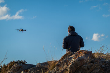 Man controlling drone with remote in nature with clear sky and rocky surroundings. The setting...