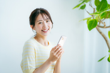 部屋でスマホを操作する女性 © wheeljack