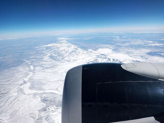 Window view of airplane flying over snowy mountains of Vancouver Canada in winter time with cold, snow and freezing