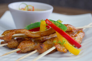 Low-angle view of vibrant glazed chicken skewers with roasted bell peppers, lemon zest, and creamy spicy mayonnaise, set against a dark blurred background.