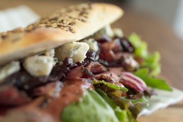 Italian panini sandwich filled with rich blue cheese, caramelized onions, roast beef and lettuce, close-up.